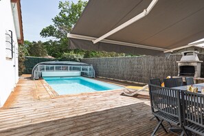 Un patio trasero con piscina, una parrilla y un porche cubierto.