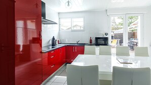 Una cocina moderna con armarios rojos, una encimera blanca y un comedor con una mesa y sillas blancas.