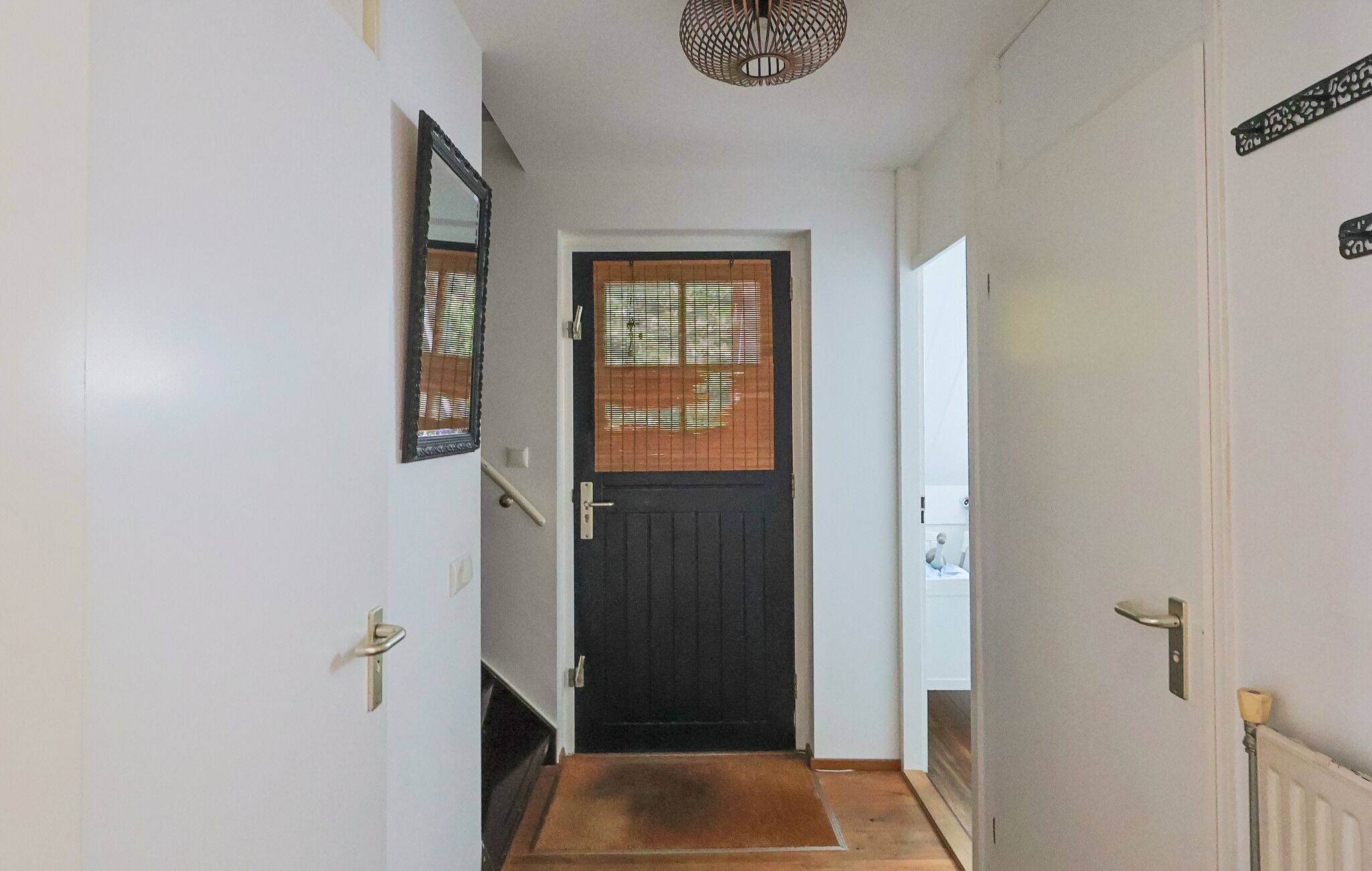 En gang med en mørk dør, et trin og en dørmåtte, der fører til et rum med en radiator.