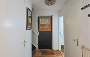 A hallway with a dark door, a small step, and a mat leading to a room with a radiator. - Luxury holiday home with private sauna in Lunteren (Lunteren)