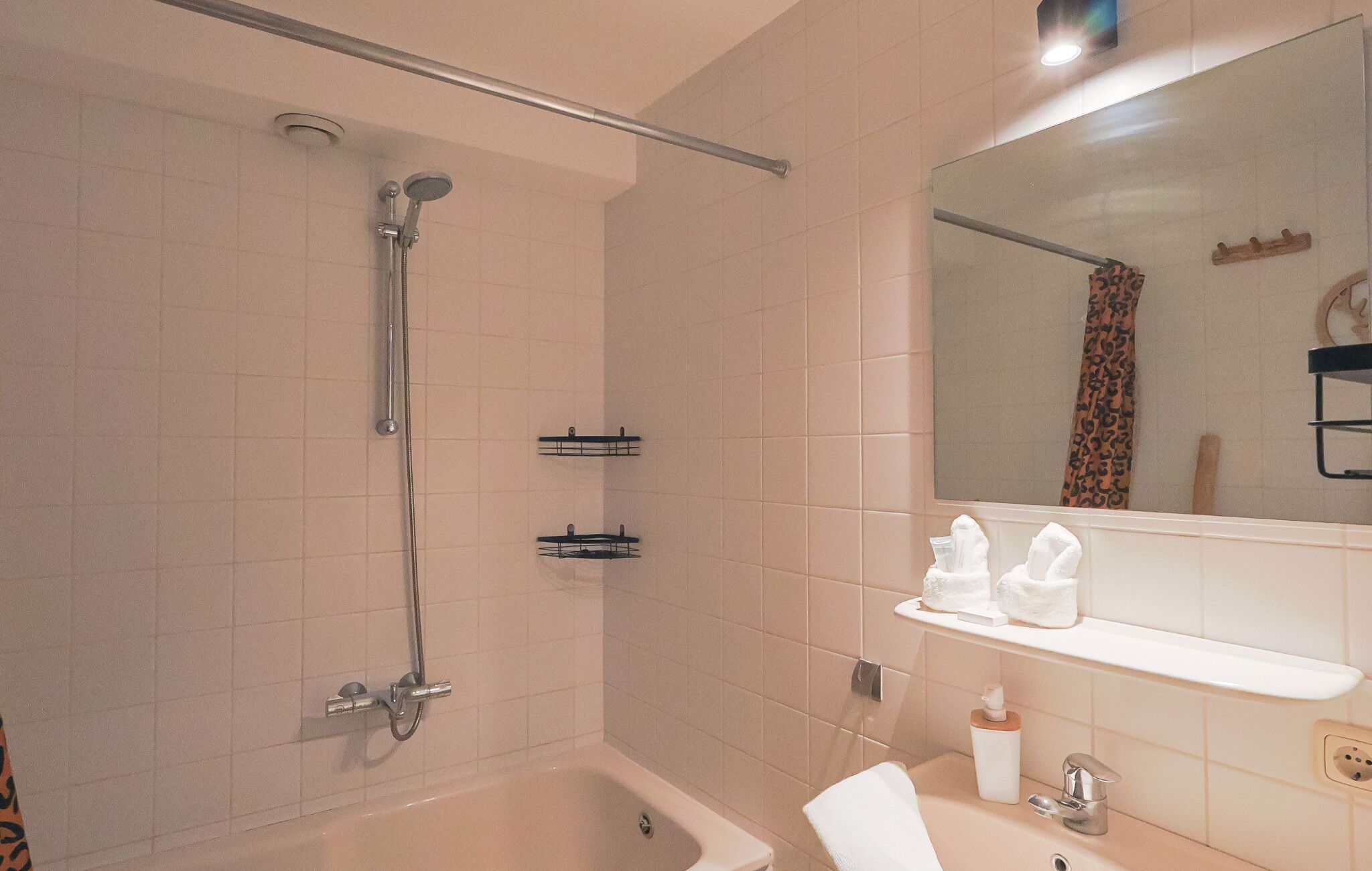 Ein Badezimmer mit Badewanne, Dusche, Spiegel und Ablage für Pflegeprodukte.