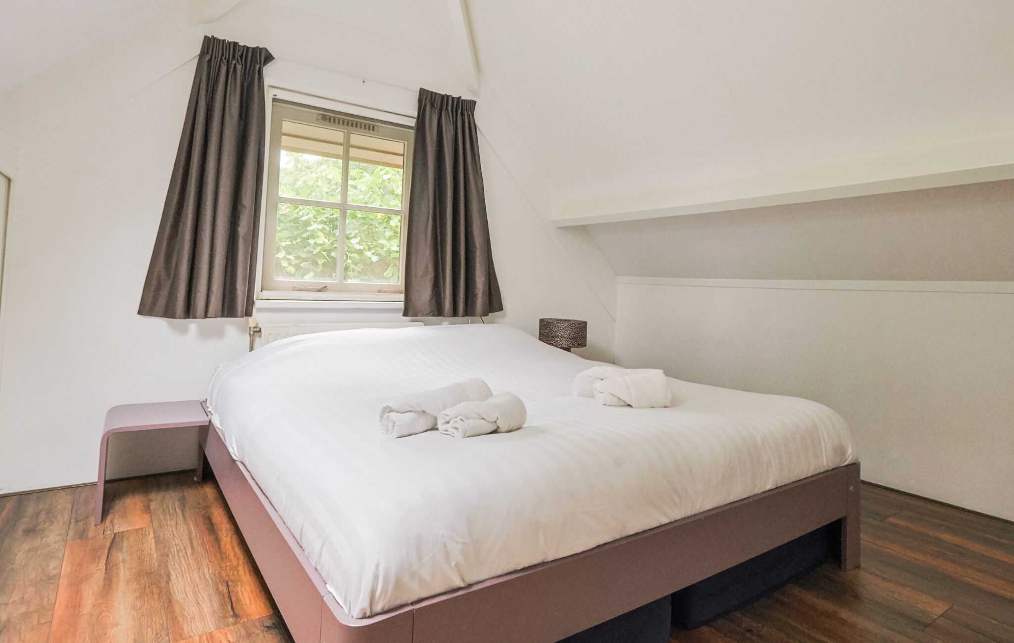 A bedroom with a bed, a window with curtains, a bedside table, and a lamp.