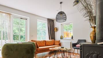 A living room with a sofa, a chair, a table, a decorative lamp, and a view of greenery outside.