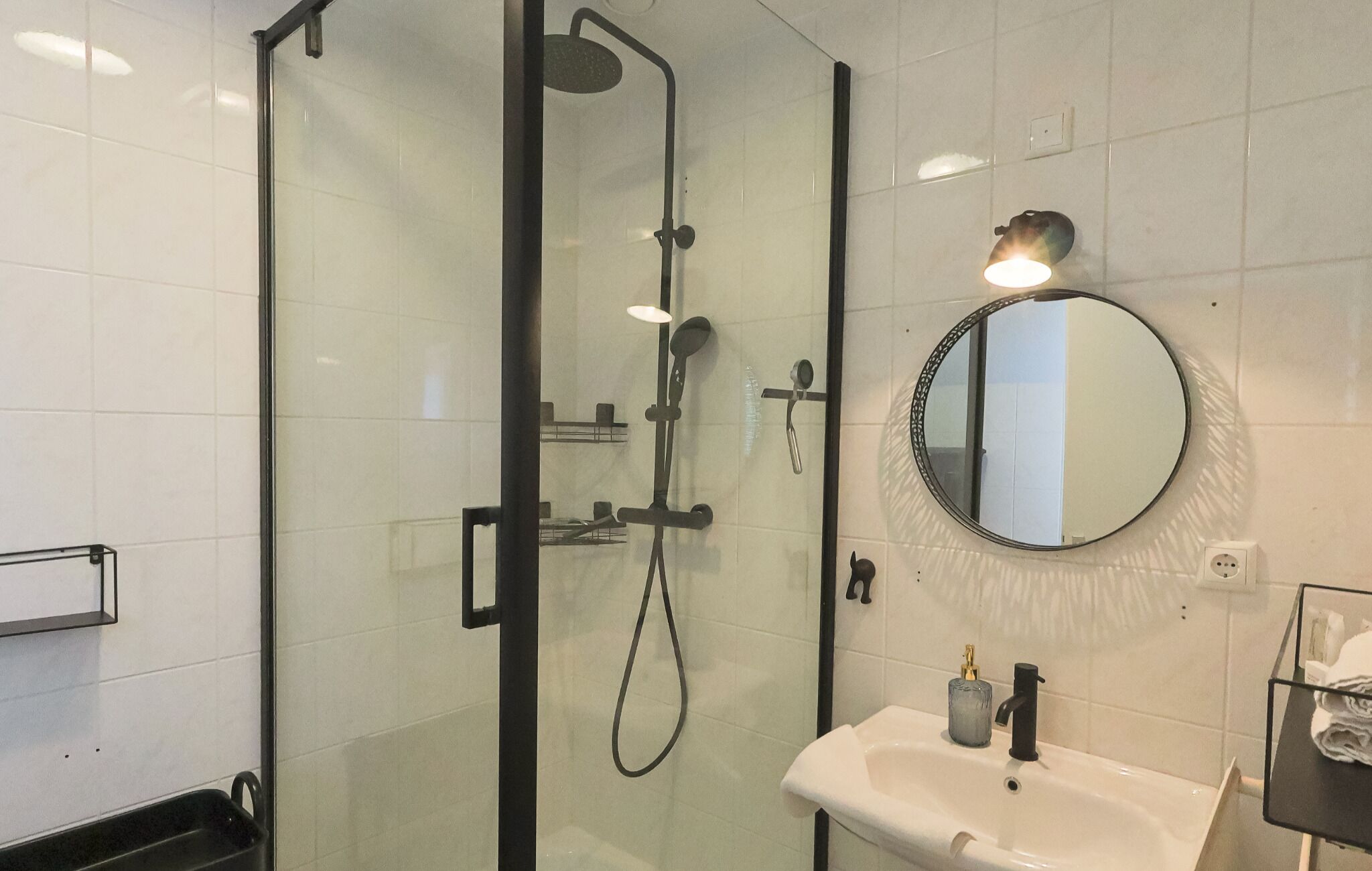 Une salle de bain moderne avec une douche à parois de verre, un miroir rond et un lavabo blanc.