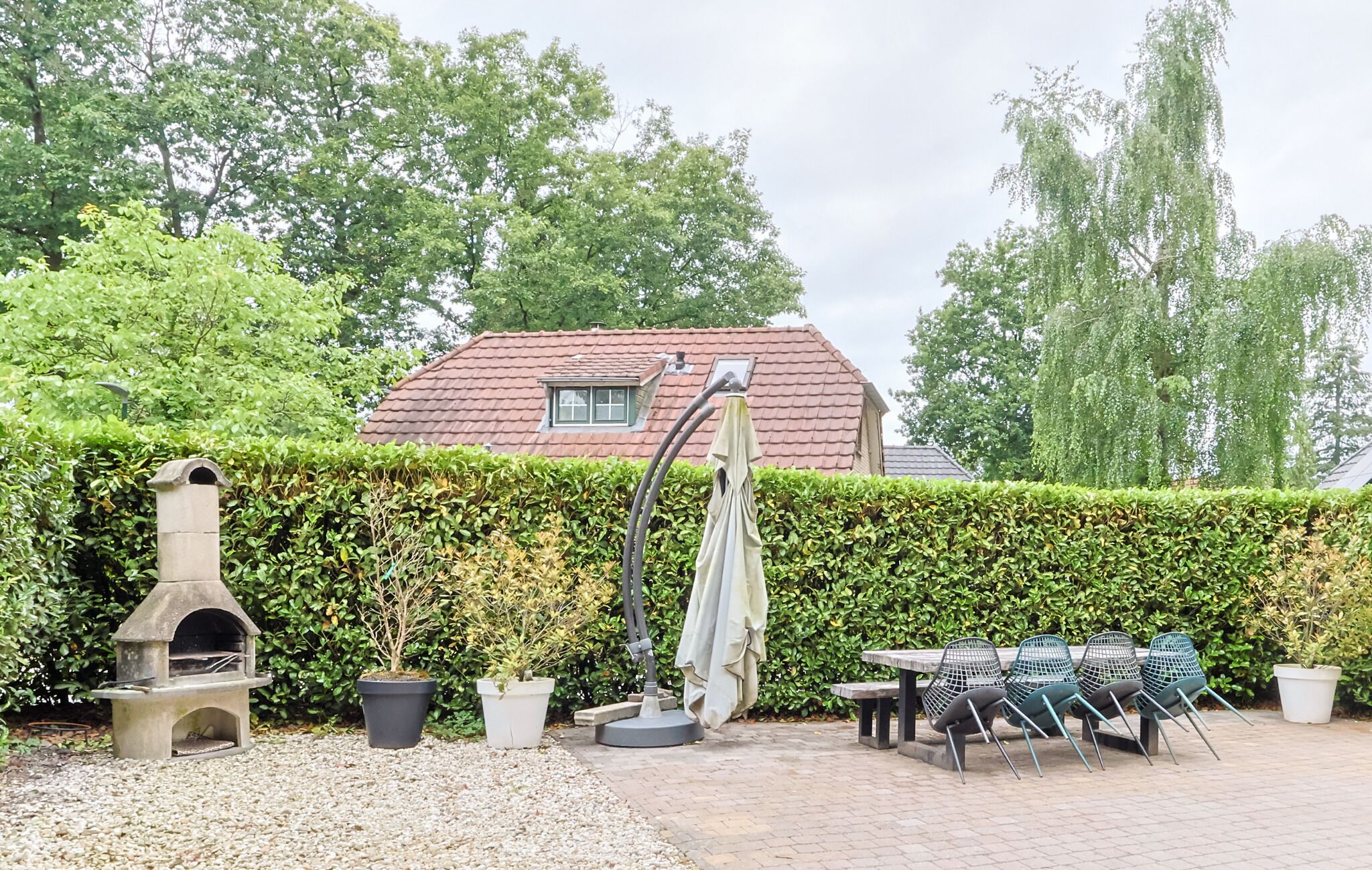 A garden with a stone oven, potted plants, outdoor furniture, and a hedge.