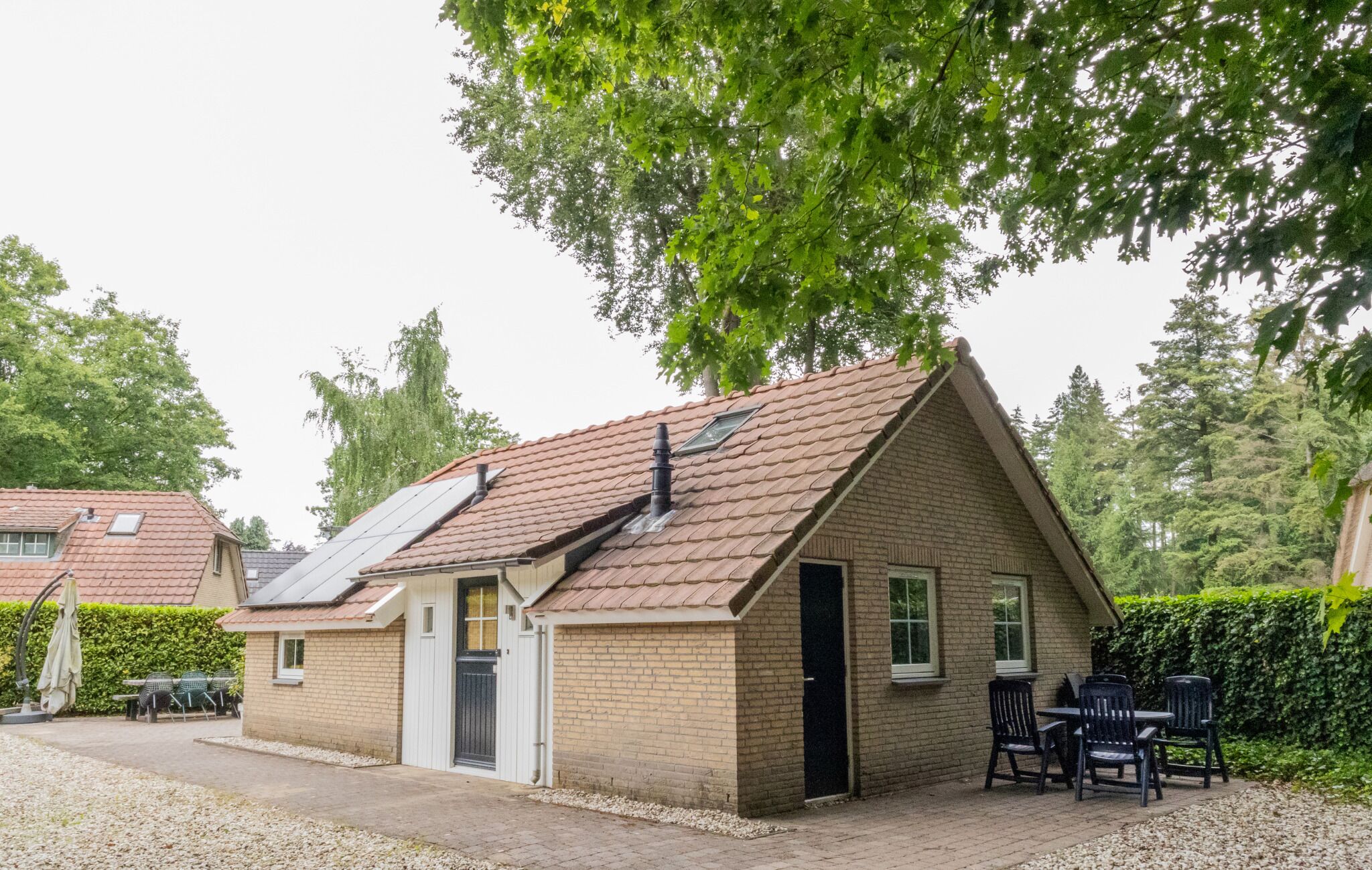 A small brick house with a sloped roof, solar panels, a door, and a small patio with chairs.