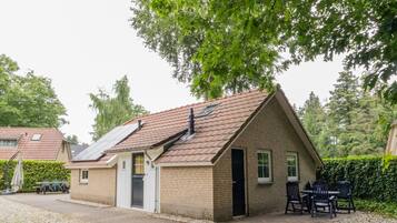 A small brick house with a sloped roof, solar panels, a door, and a small patio with chairs.