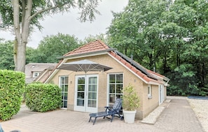 En liten byggnad av tegel med ett sluttande tak, en entré med glasdörr, en fåtölj och en krukväxt.