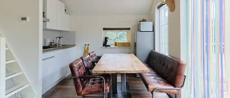 Een moderne keuken met een eethoek, met een houten tafel en lederen stoelen, een inbouwoven en een raam met uitzicht.