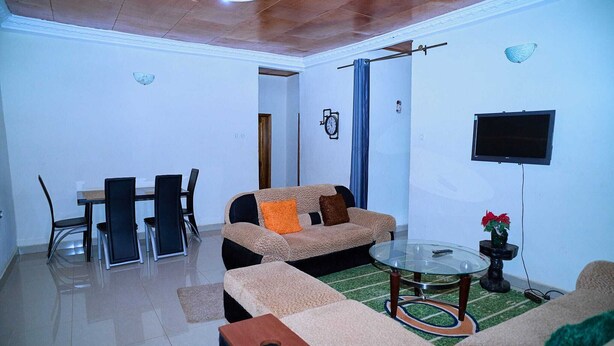 Una sala de estar con un sofá, sillas, una mesa de vidrio, un televisor y un reloj en la pared.