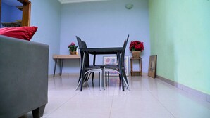 Una habitación con un sofá gris, una mesa de comedor negra con sillas, una pequeña mesita de madera con un florero y un cuadro en la pared.