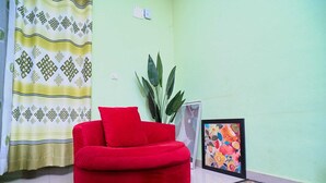 Un sofá rojo, una planta en maceta, un cuadro enmarcado y una cortina estampada en una habitación con paredes verde claro.