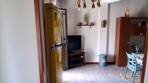 An open doorway to a living area with a television, a trash bin, and a dining area with a table and chairs. - Villa oleanders sea of sicily (Agnone)