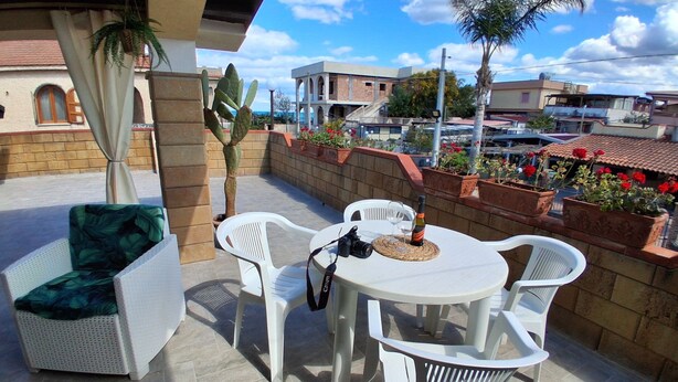 A patio with a table and chairs, a camera, and a bottle of wine. - Villa oleanders sea of sicily (Agnone)