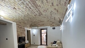 A dining area with a wooden table and white chairs, a brick ceiling, and a sofa in the background. - Suite room with private en suite bathroom and terrace (Spoltore)