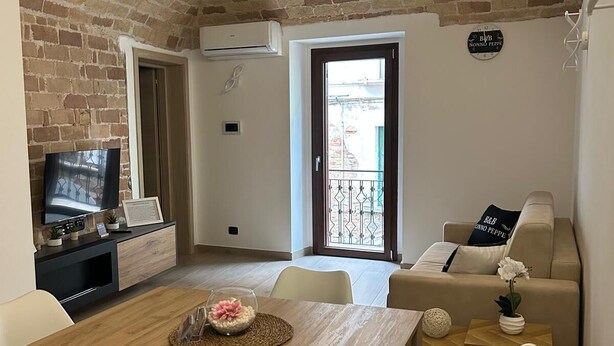 A cozy living room with a brick ceiling, a wooden dining table, white chairs, a beige sofa, and a television on a black cabinet. - Suite room with private en suite bathroom and terrace (Spoltore)