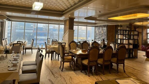 A dining area with tables and chairs, a chandelier, and a view through large windows. - Sea Shell Palace (Dhaka)