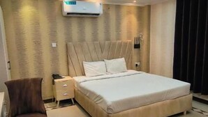 A modern bedroom with a large bed, an air conditioning unit, a nightstand, and a chair. - Sea Shell Palace (Dhaka)