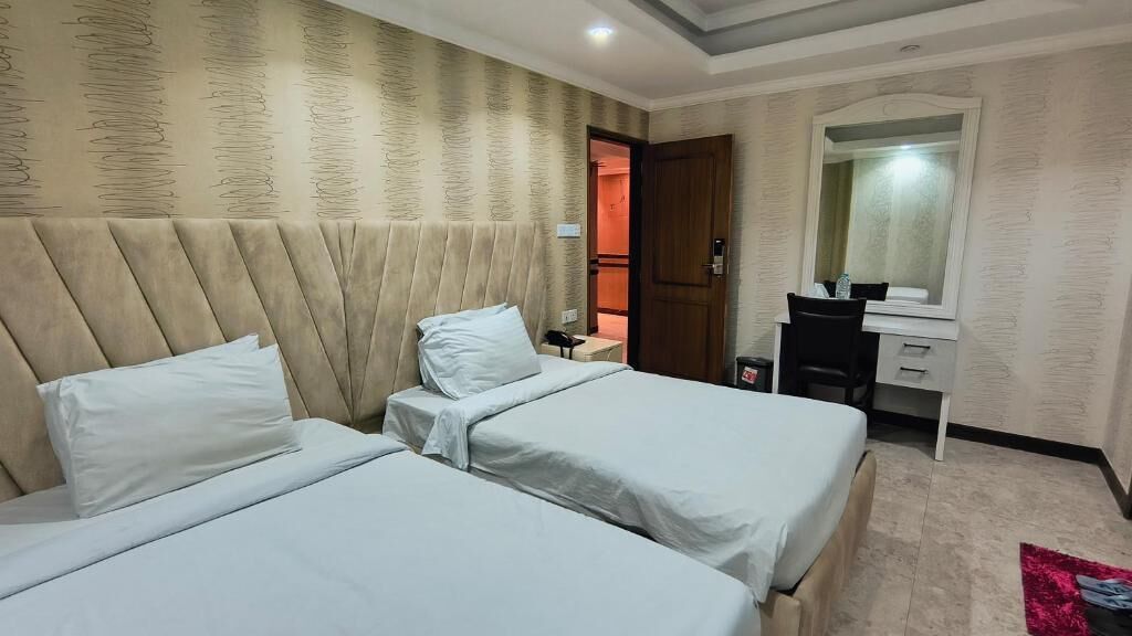 Habitación de hotel con dos camas, un escritorio, un espejo y una puerta que da a otra habitación.
