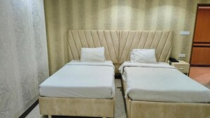 A hotel room with two single beds, a headboard, a nightstand, and a wall with a patterned wallpaper. - Sea Shell Palace (Dhaka)