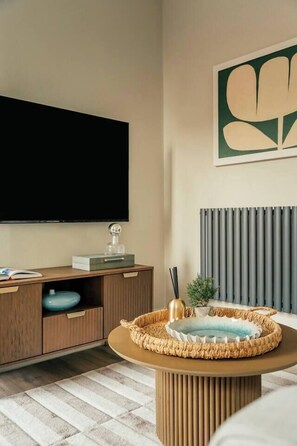 Uma sala de estar moderna com uma televisão de tela plana, um armário de madeira, uma mesa de centro redonda e uma obra de arte pendurada na parede.