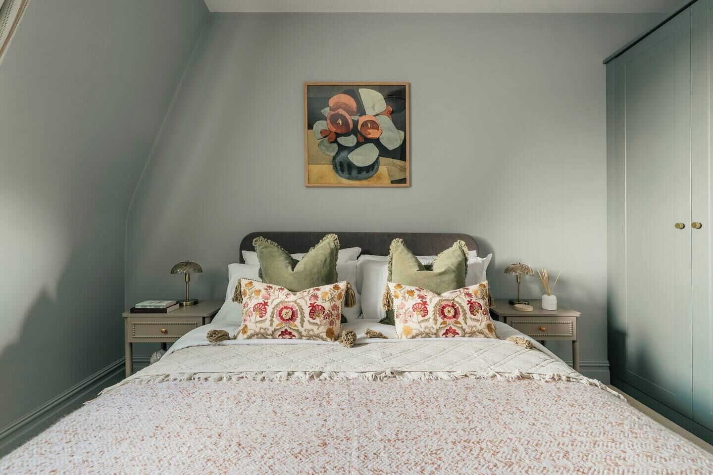 Un dormitorio con cama, dos mesitas de noche, un tocador, un cuadro en la pared y un armario.