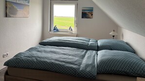 A bedroom with a bed, a window with a view of a field, and two paintings on the wall. - Huus Diekblick Ditzum (Bunde)