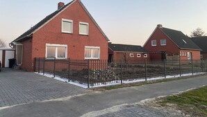 A red brick house with a black metal fence, a paved driveway, and a clear sky. - Huus Diekblick Ditzum (Bunde)