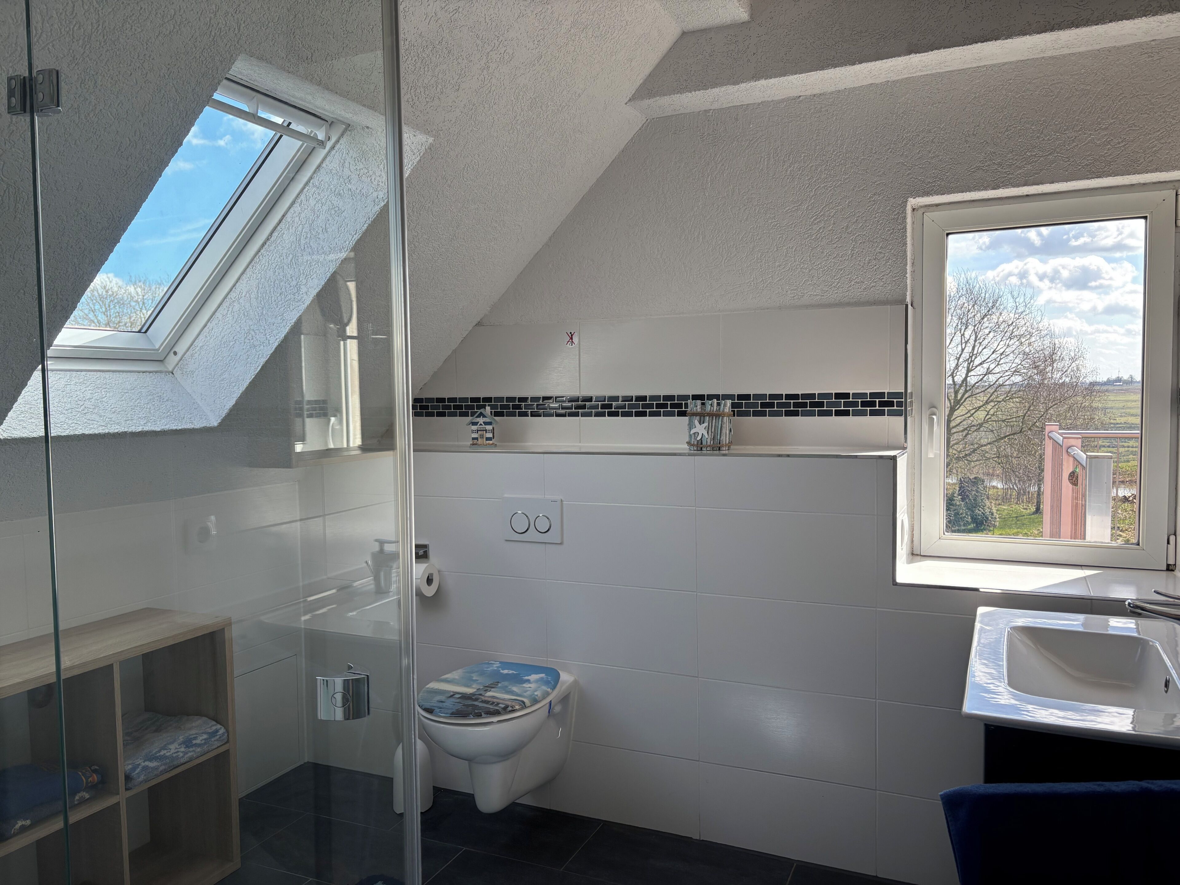 A modern bathroom with a skylight, a toilet with a decorative seat, a sink, and a window with a view of the outdoors.