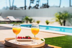 Two glasses of orange juice on a tray with strawberries and blueberries, by a pool with lounge chairs and palm trees in the background. - OCEANBREEZE AROEIRA - Optional heated pool - Just 5 minutes from the beach (Aroeira)