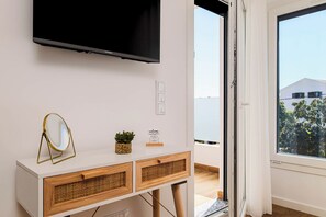 Una habitación con una televisión en la pared, una mesita con un espejo y una planta, y vista al exterior a través de una puerta.