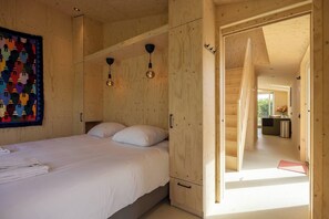 Une pièce en bois avec un lit, une armoire et une porte donnant sur une autre pièce.