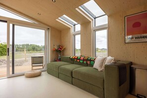 Un intérieur moderne avec un canapé vert, un petit pouf rond, un vase de fleurs et une affiche accrochée au mur.