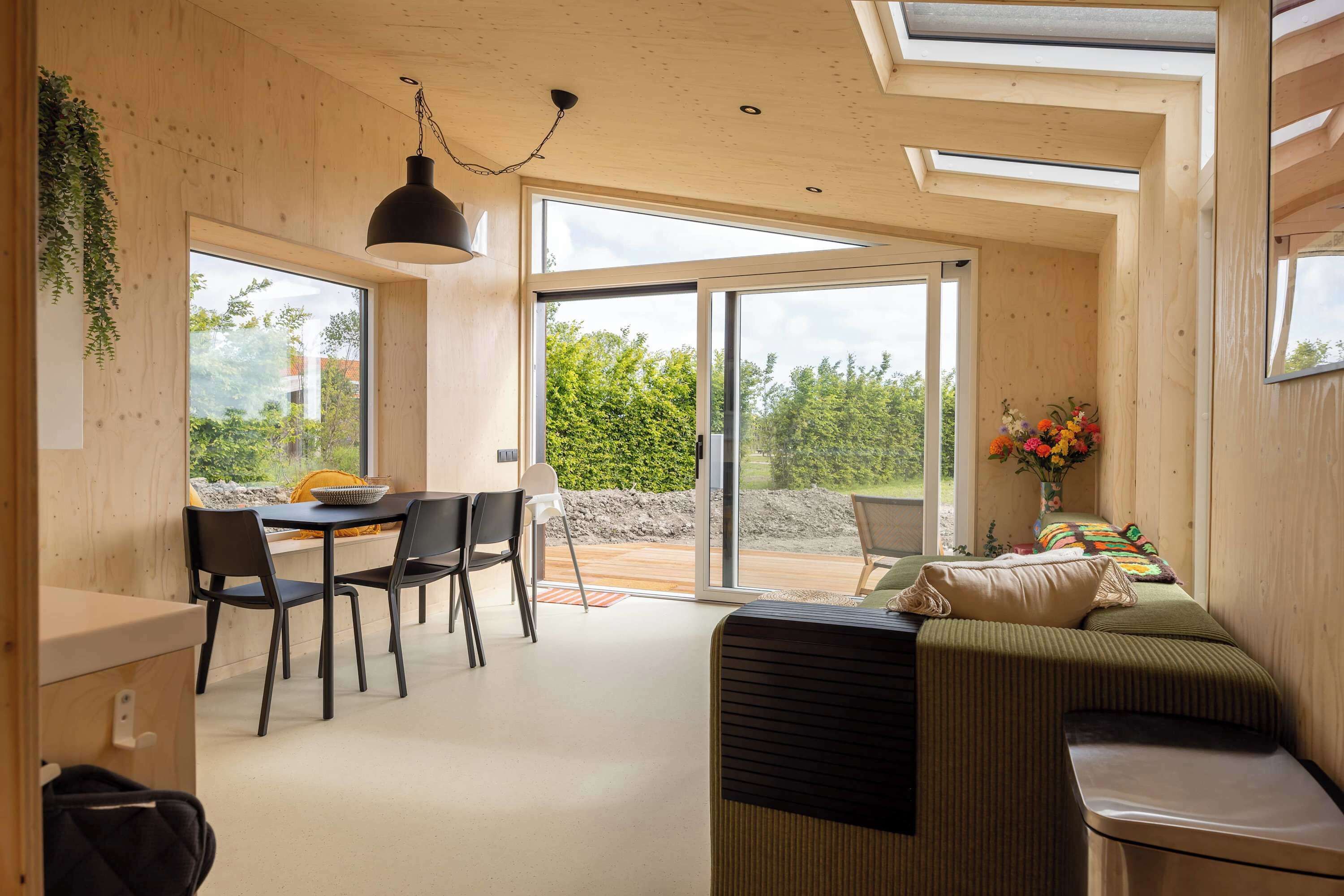 Un intérieur moderne comprenant un coin repas, un canapé et une grande porte-fenêtre coulissante donnant sur un espace extérieur.