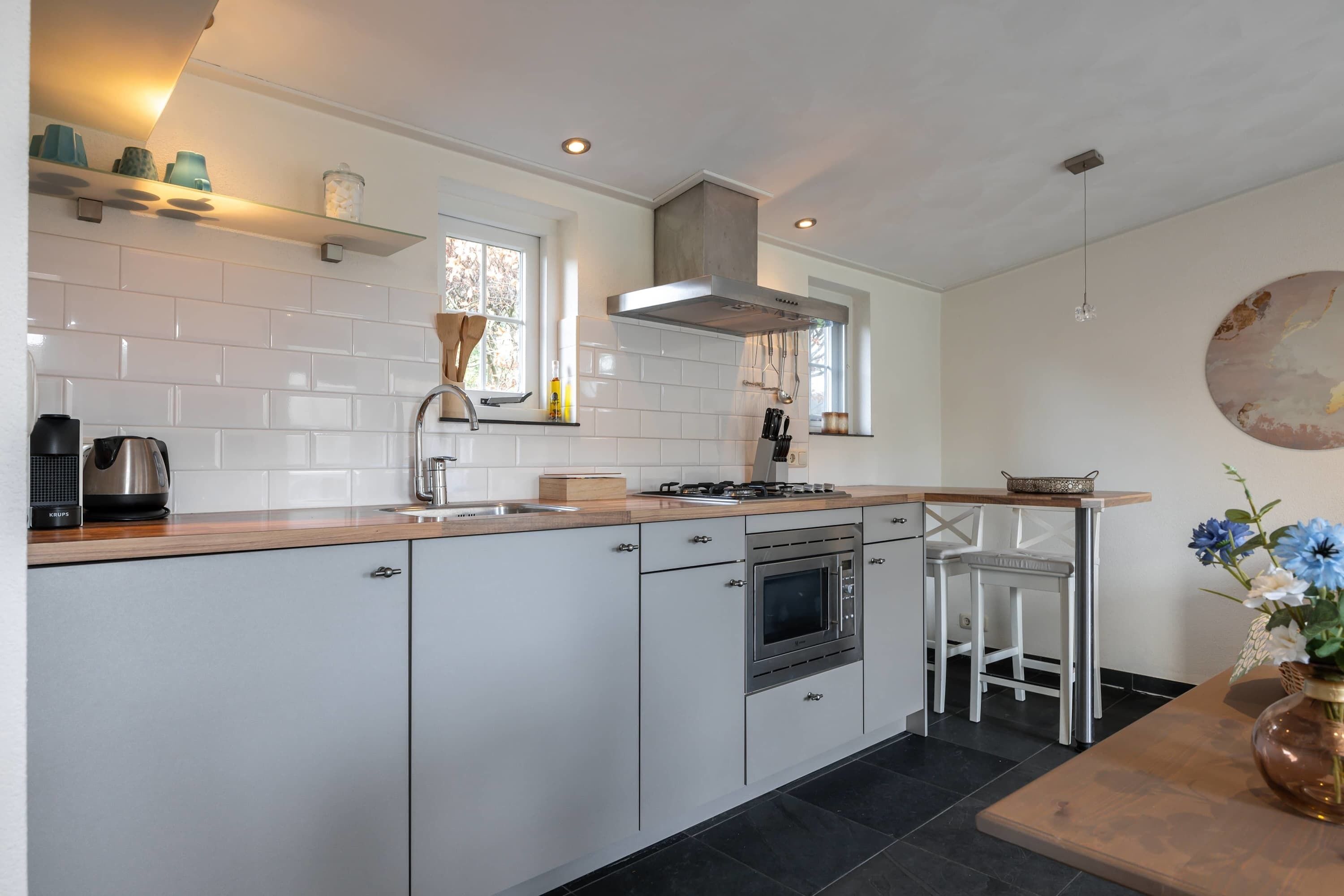 A modern kitchen with white cabinets, a stainless steel range, a built-in oven, a window, and a bar stool.