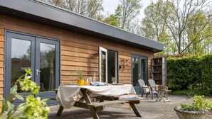 Ein Holzhaus mit einer Terrasse, einem Tisch mit Stühlen und einem Garten.