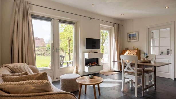 Ein Wohnzimmer mit Sofa, Hocker, Fernseher, Kamin, Esstisch und Stühlen.