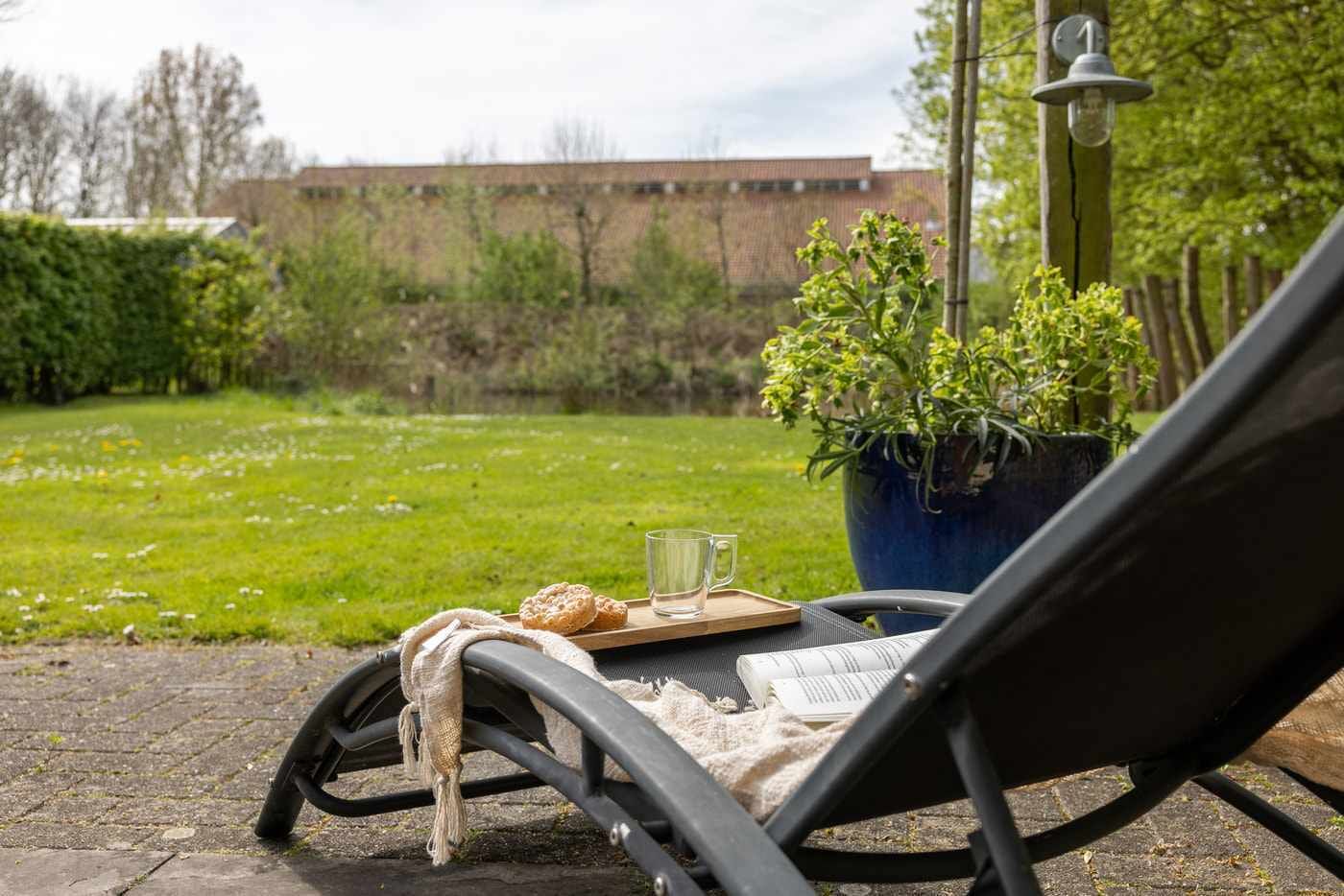 Een uitzicht op een tuin met een stoel, een dienblad met gebak, een glas en een boek.
