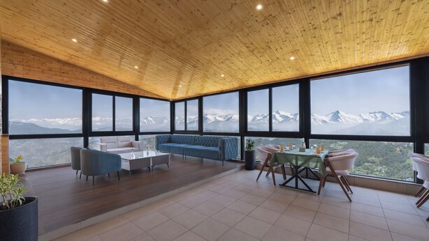 Una habitación amplia con techo de madera, ventanas grandes, un sofá azul, una mesa de comedor y sillas.