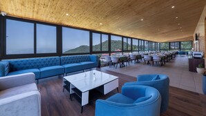 Un espacio interior amplio con techo de madera, ventanas grandes que ofrecen vistas al exterior, un sofá azul y una mesa de centro blanca.
