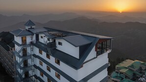 Un hotel de varios pisos con terraza en la azotea, varios balcones y vistas a montañas distantes.