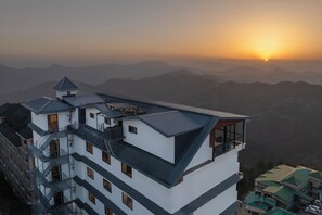 Un immeuble à plusieurs étages doté d’une terrasse sur le toit, d’une échelle de secours et offrant une vue sur les montagnes lointaines.