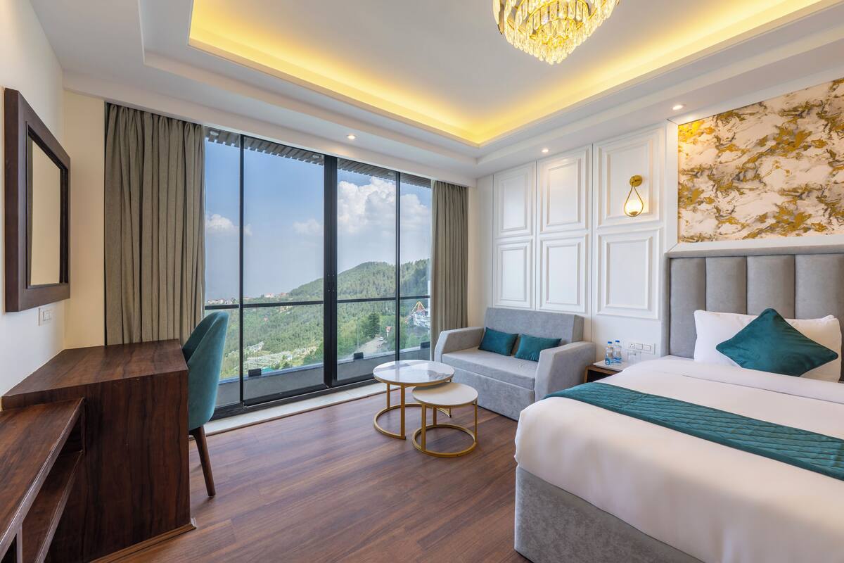 Een hotelkamer met een groot raam, een bureau, een bank, een bed en een kroonluchter.