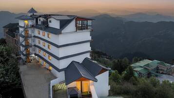 A multi-story hotel with a balcony on the upper floor, a staircase, and a view of the surrounding mountains.