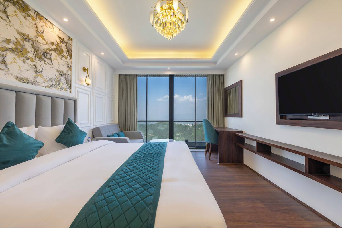 Een hotelkamer met een groot bed, een televisie, een bureau en uitzicht op de stad.