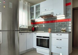 Eine moderne Küche mit weißen Schränken, einem Edelstahlkühlschrank, einem eingebauten Ofen und einer roten Küchenwand.