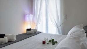 Hotellihuone, jossa on sänky, yöpöytä, jossa on pyyhkeitä, lamppu ja ikkuna, jossa on ohuet verhot.