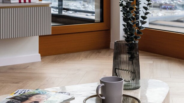 Una habitación moderna con un ventanal grande, un radiador, una revista, una taza y una planta.