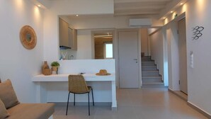 A modern hotel room with a white console table, a chair, a sofa, and a staircase leading to another area. - KAELA Pool Villas (Agios Nikolaos)