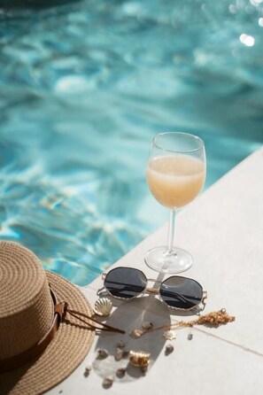 Une scène de bord de piscine, avec un verre à la main, des lunettes de soleil et un chapeau de paille.